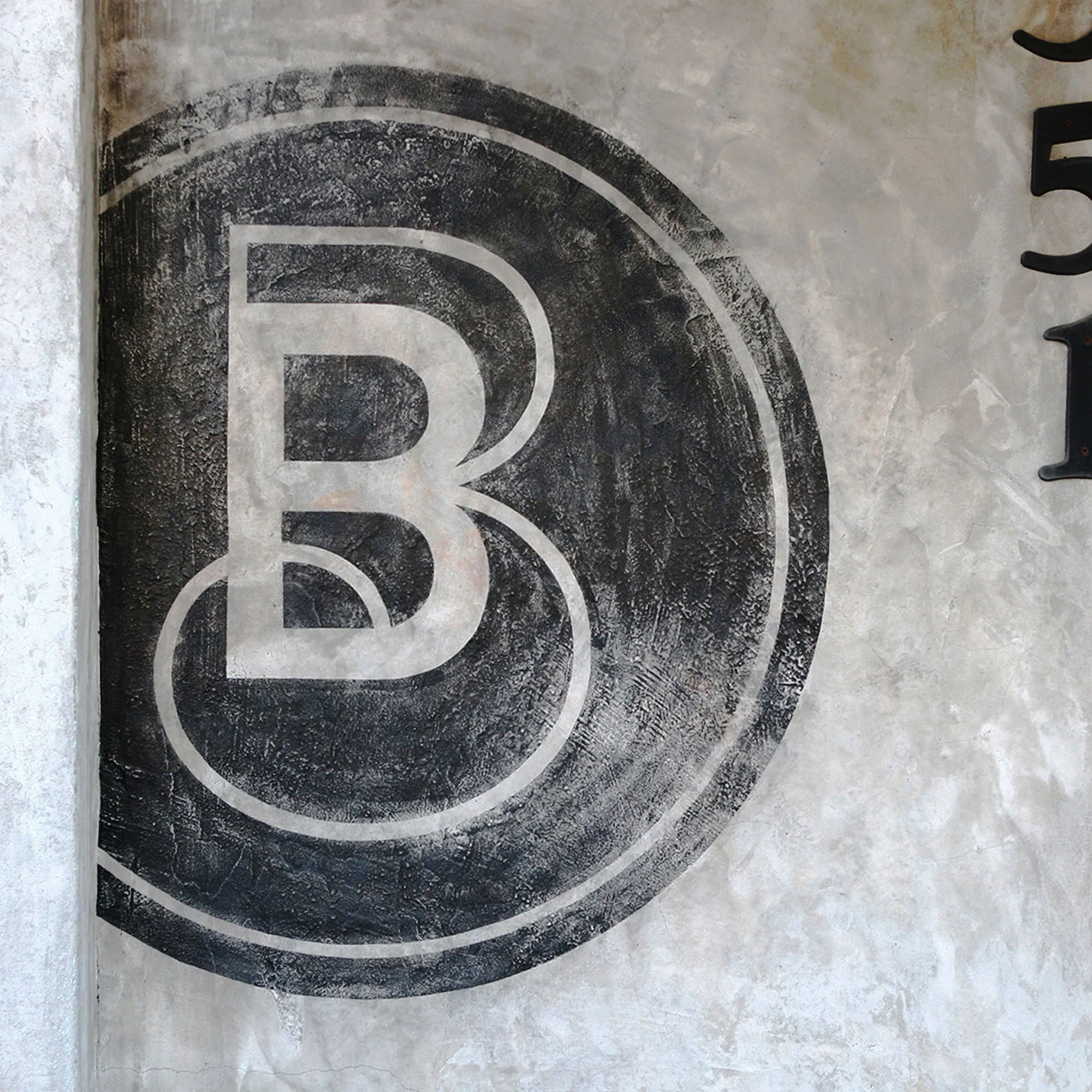 Blue Butterfly Coffee Co. monogram painted on a weathered concrete wall.