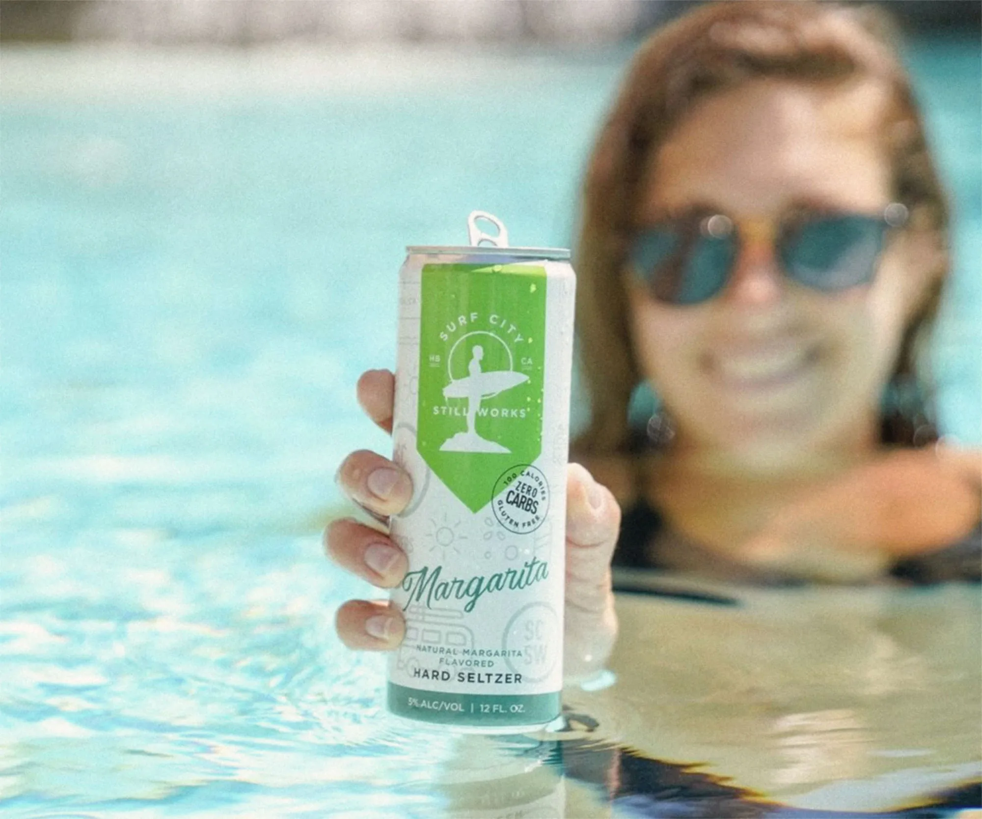 Woman in a pool holding a Surf City margarita hard seltzer can.